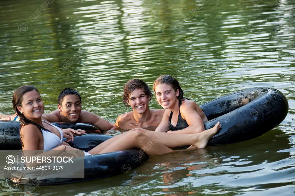 A group of young people, boys and girls, swimming and floating using swim floats and inflated tyres. Maryland, USA. 7/1/2012