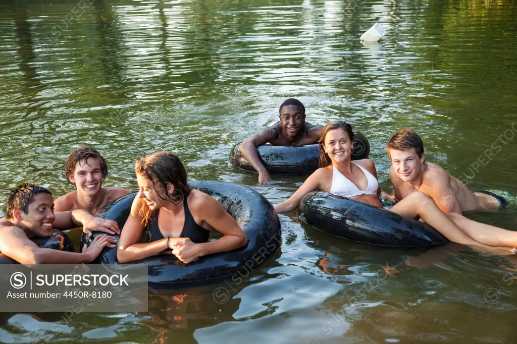 A group of young people, boys and girls, swimming and floating using swim floats and inflated tyres. Maryland, USA. 7/1/2012