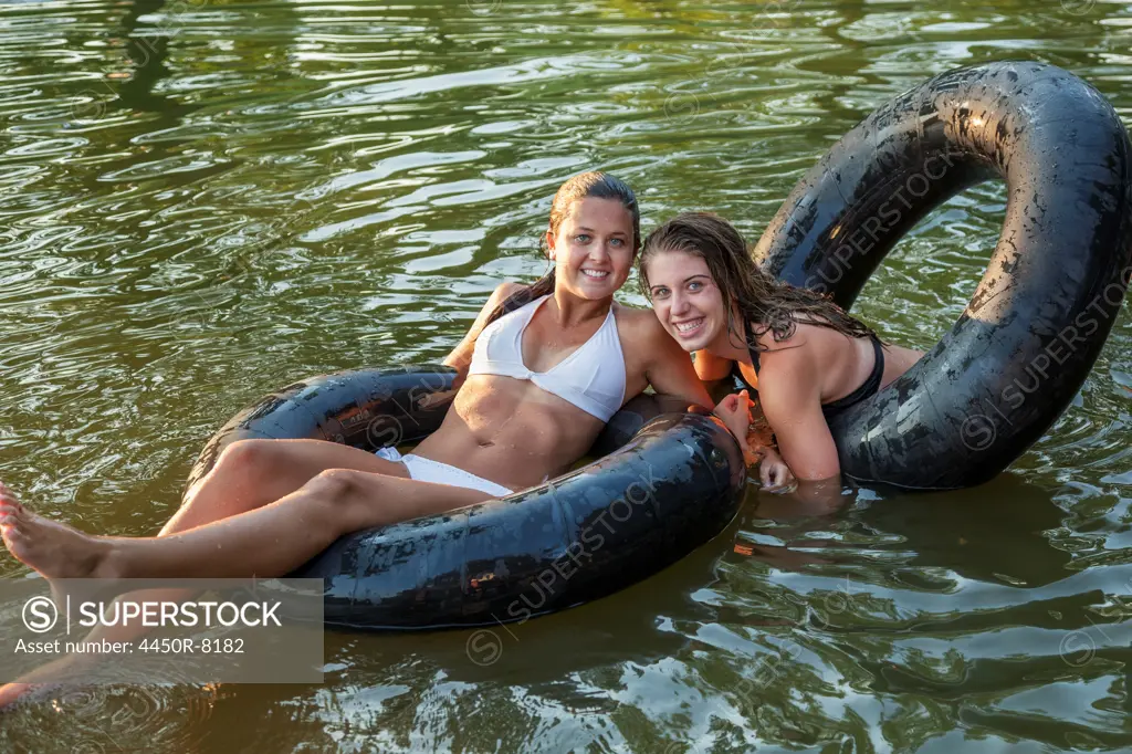 Two girls swimming and floating using swim floats and inflated tyres. Maryland, USA. 7/1/2012