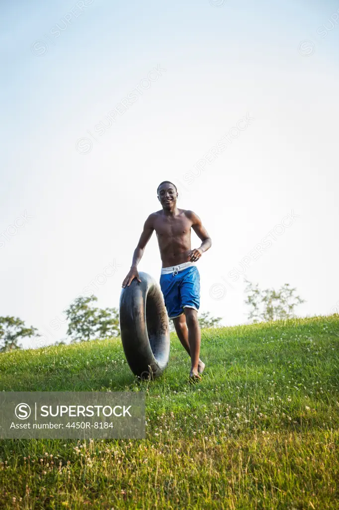 A teenage boy running across the grass rolling a swim float, black tyre in front of him. Maryland, USA. 7/1/2012