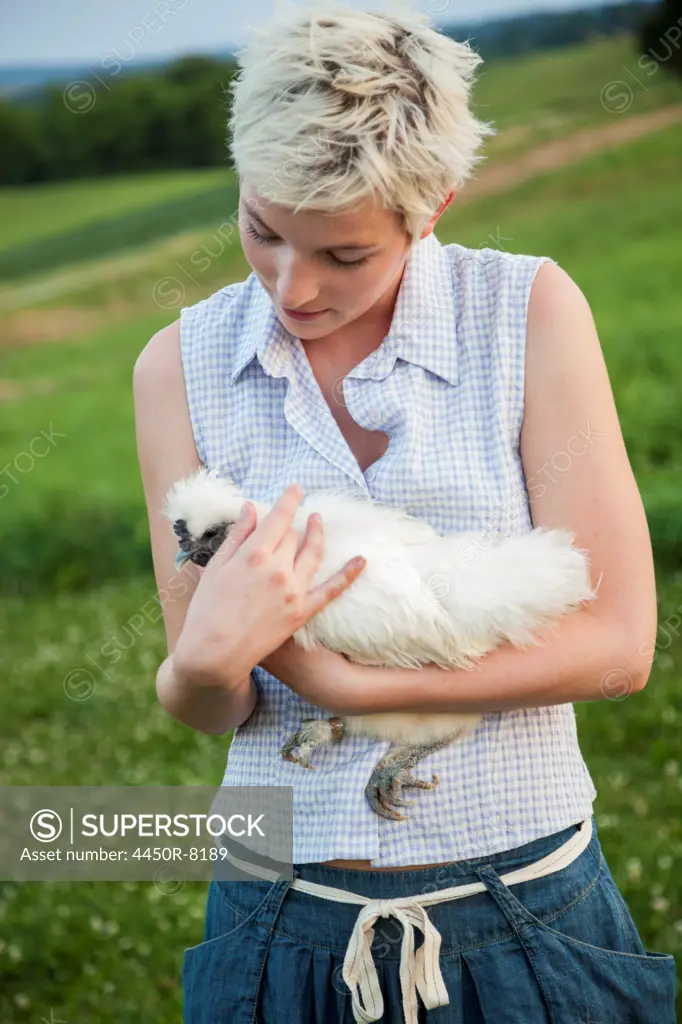 A young girl, teenager, holding a chicken with white feathers in her arms. Maryland, USA. 7/1/2012