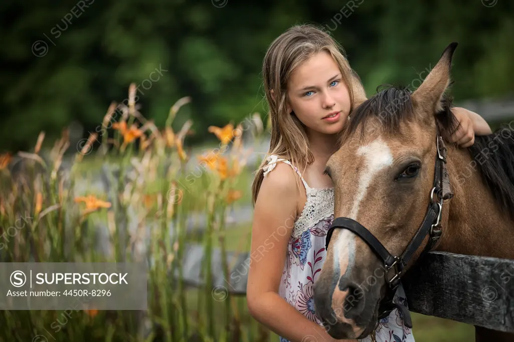 A young girl with a pony wearing a halter, in a field full of wild flowers and grasses. New York state, USA. 3/22/2012
