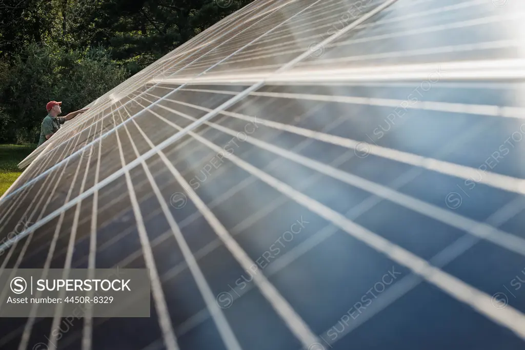 A man inspecting the surface of a large tilted solar panel installation for harnessing the energy of the sun. New York state, USA. 3/23/2012