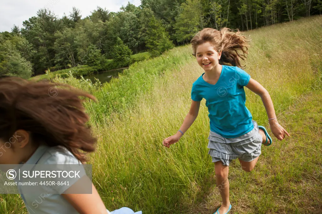 Two children, girls playing chase and running along a path. New York state, USA. 6/26/2012