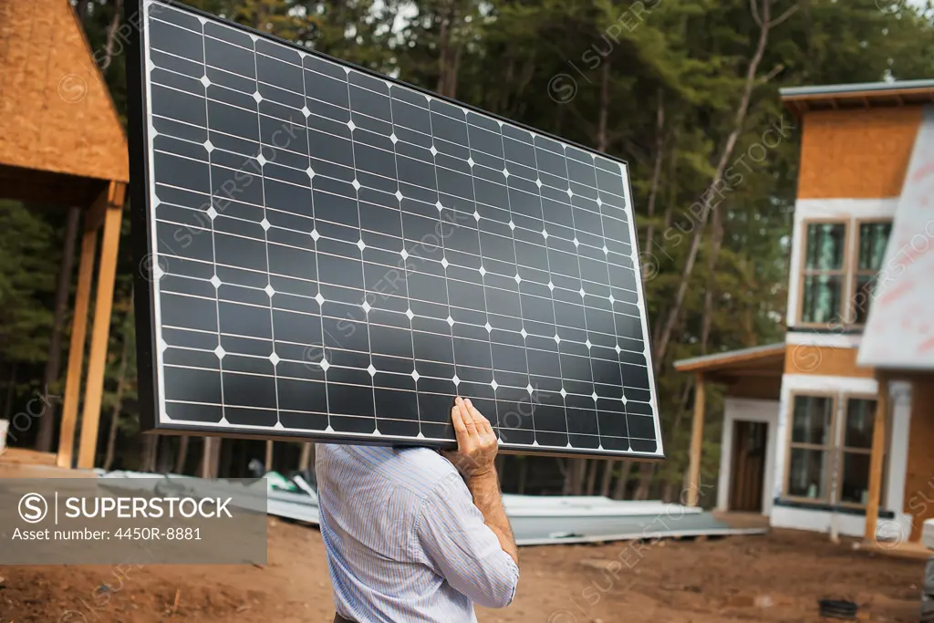 A workman carrying a large solar panel at a green house construction site. Woodstock, New York, USA. 4/27/2012