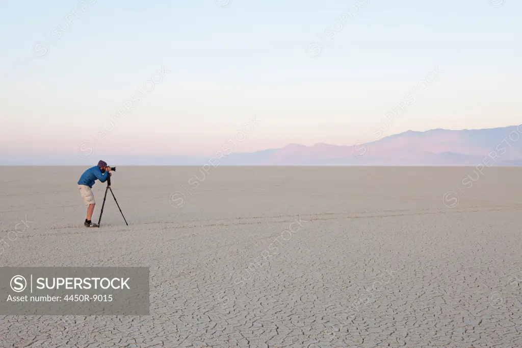 Man with camera and tripod on the flat saltpan or playa of Black Rock desert, Nevada. Black Rock Desert, Nevada, USA. 8/8/2012