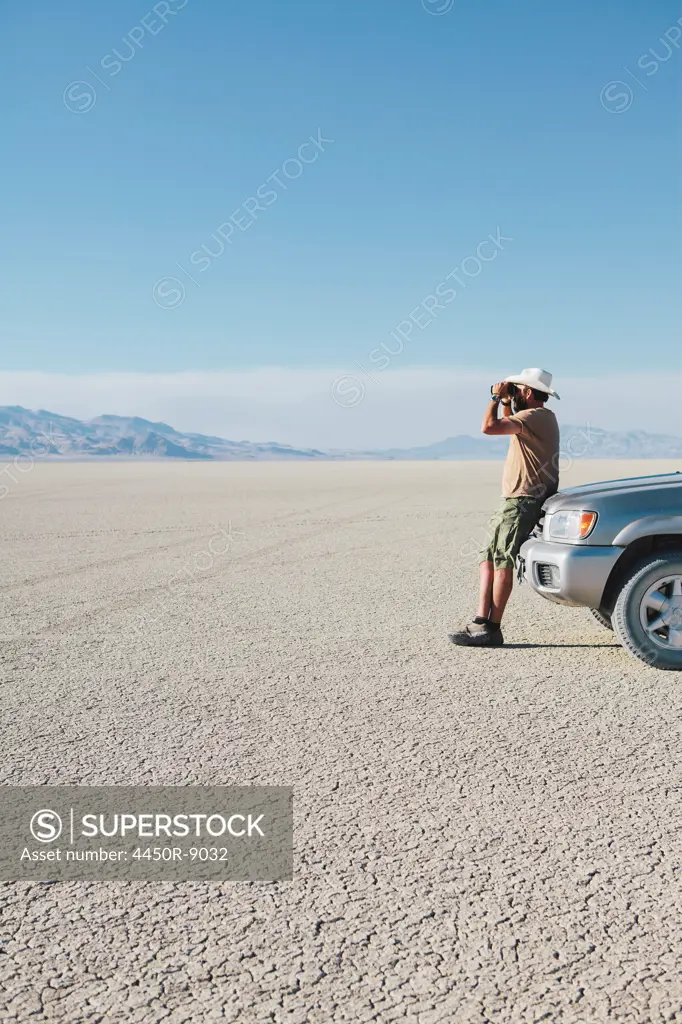 A man leaning against a truck, looking through binoculars. Black Rock Desert, Nevada, USA. 8/8/2012