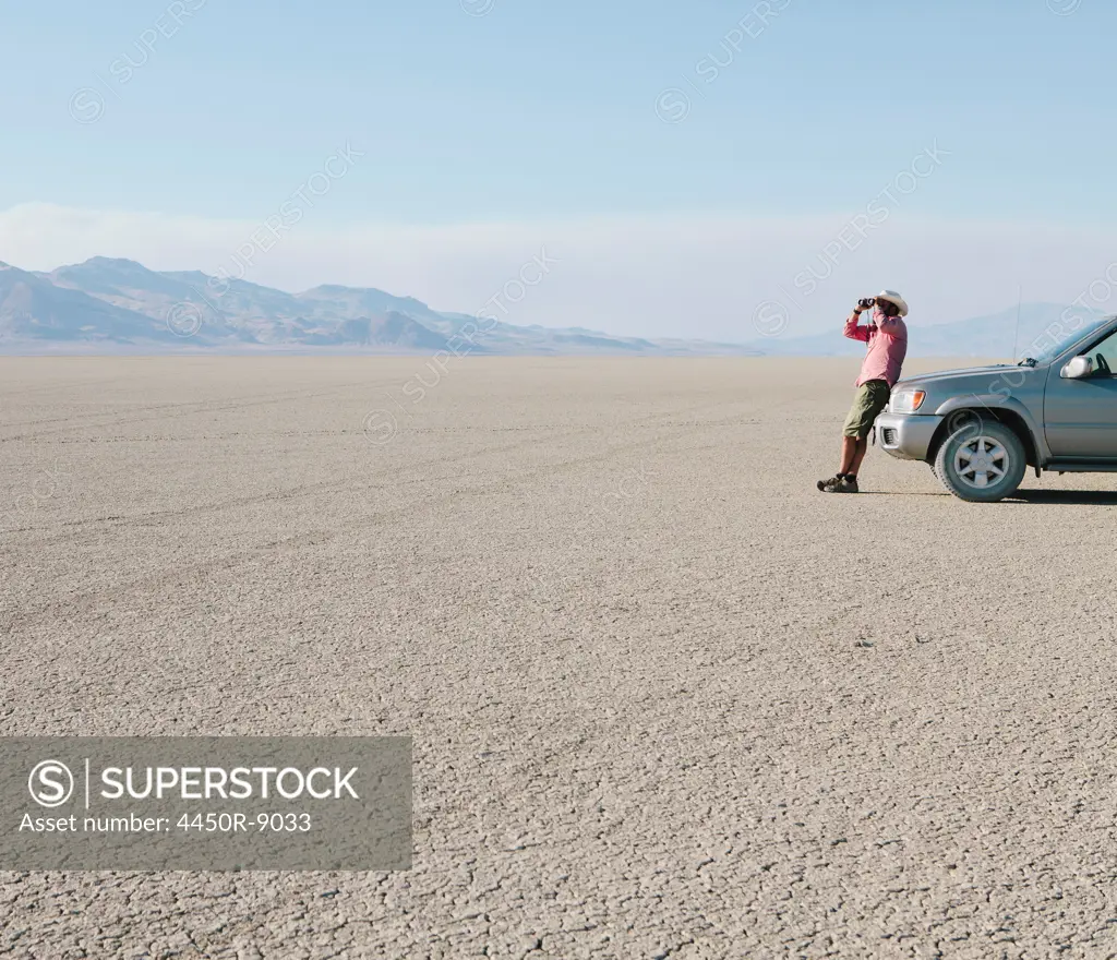 A man leaning against a truck, looking through binoculars. Black Rock Desert, Nevada, USA. 8/8/2012