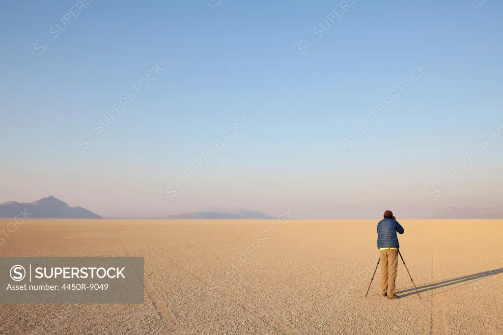 Man with camera and tripod on the flat saltpan or playa of Black Rock desert, Nevada. Black Rock Desert, Nevada, USA. 8/9/2012