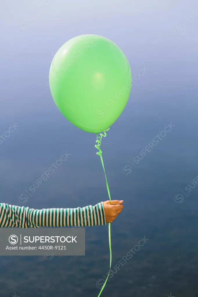 Nine year old girl holding green balloon, sitting by waters edge, Seattle, Washington, USA. 9/22/2012
