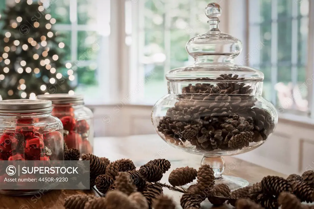 A decorative glass jar of pine cones and red glass baubles on a table top. Christmas decorations. Woodstock, New York, USA. 9/9/2012
