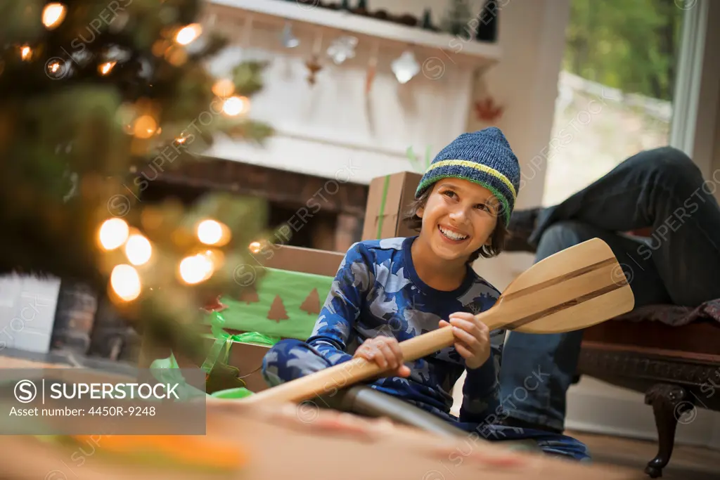 A boy by a Christmas tree unwrapping a gift, a wooden oar. Woodstock, New York, USA. 9/9/2012