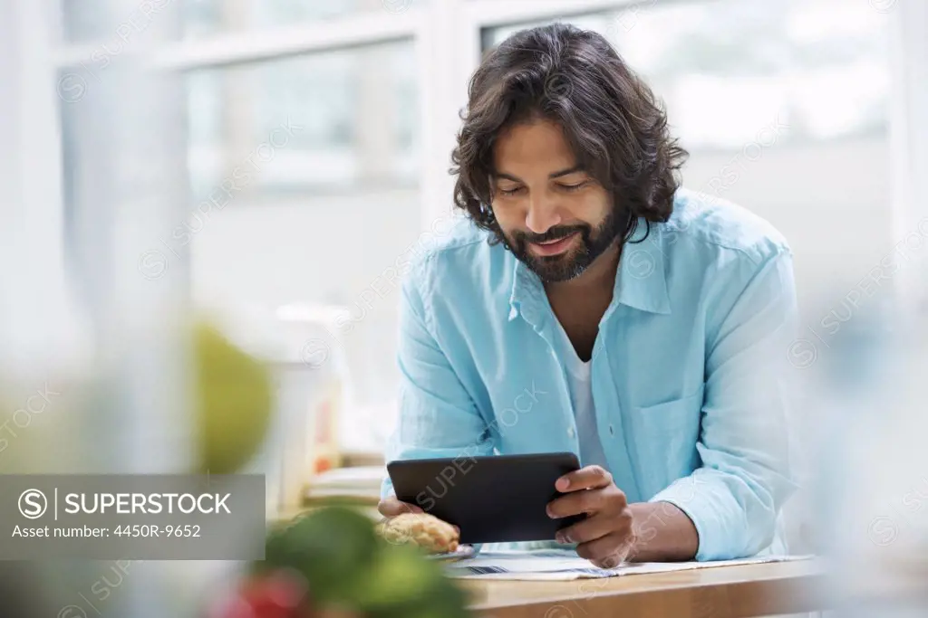 An office or apartment interior in New York City. A bearded man in a turquoise shirt using a digital tablet.  New York City, USA