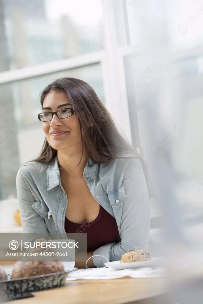 An office or apartment interior in New York City. A young woman with long black hair, having a cup of coffee. New York City, USA