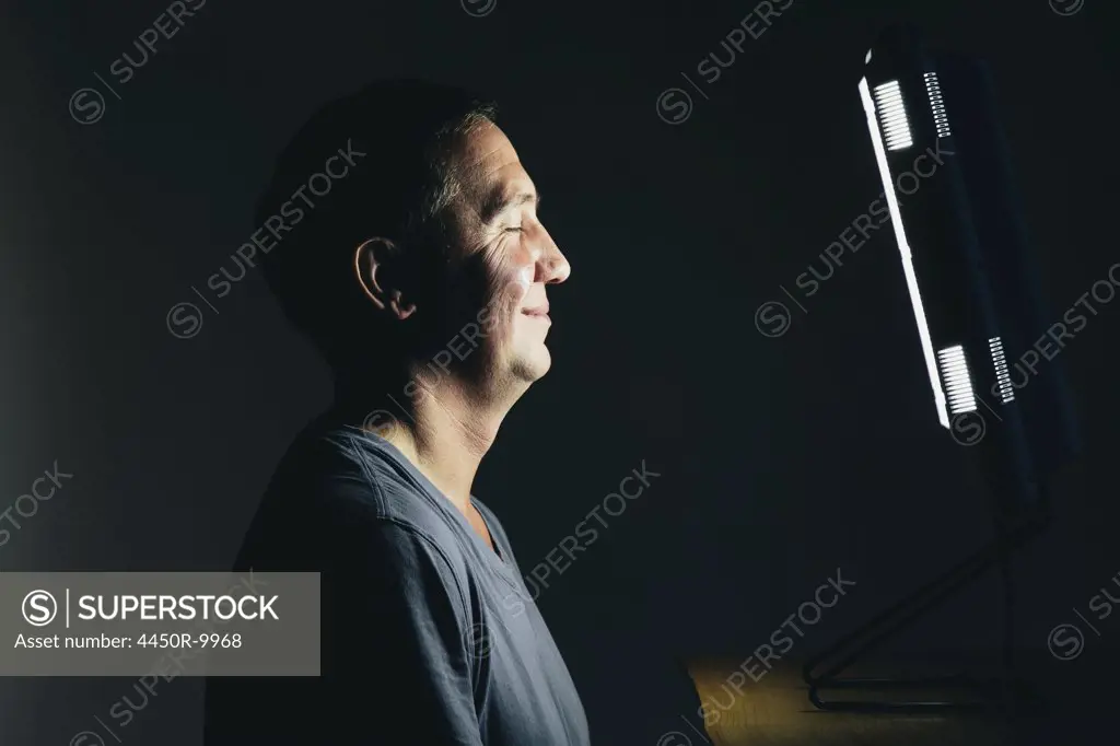 Smiling middle aged man sitting in front of a light therapy box, a full spectrum light box which mimics the sun, and treats people suffering from seasonal affective disorder.King County, Washington, USA
