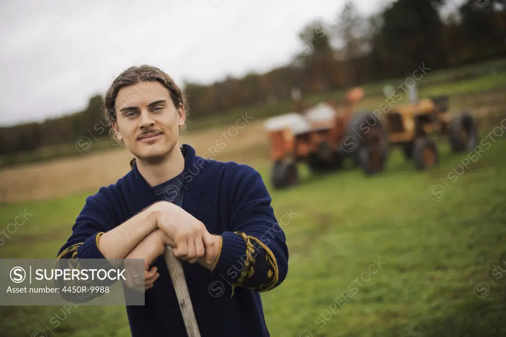 Organic Farmer at Work, A man leaning on a garden hoe. A tractor in the background.Accord, New York, USA