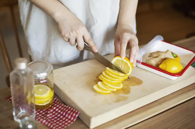 High angle close up of person cutting lemon with knife on wooden cutting board.