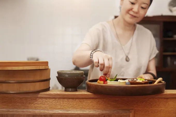 Japanese woman preparing fresh vegetables in a vegetarian cafe.