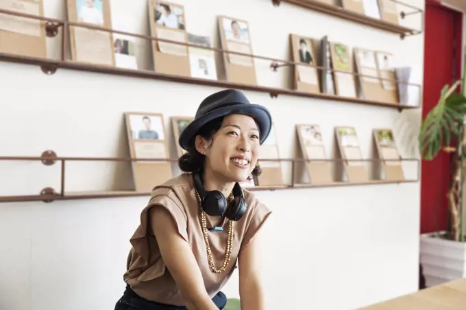 Female Japanese professional wearing Trilby hat and headphones sitting  in a co-working space.