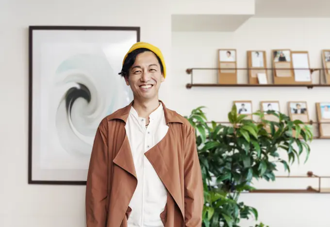 Male Japanese professional standing in a co-working space, smiling at camera.