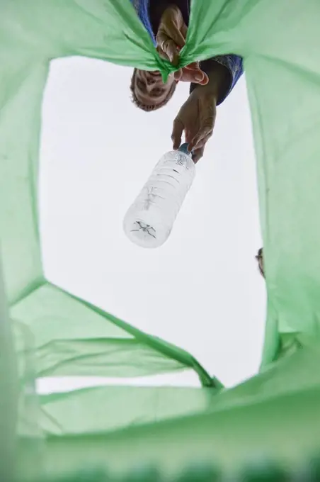 Man dropping a plastic bottle into a green plastic bag, view from inside bag. 