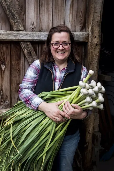 Smiling woman holding bunch of freshly picked garlic.
