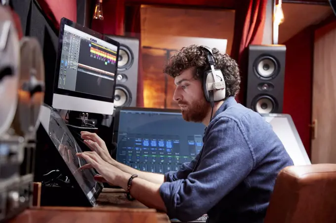 Man working in music studio using computer wearing head phones