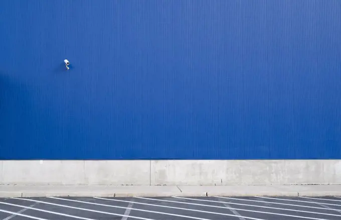Surveillance camera on a blue exterior wall of warehouse or large windowless building.