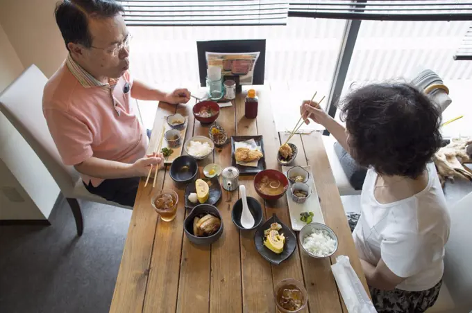 Woman and man sitting at a table, eating Japanese Food with chopsticks.