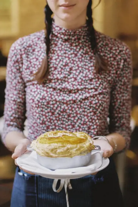 A woman carrying a fresh baked pastry topped pie on a plate.
