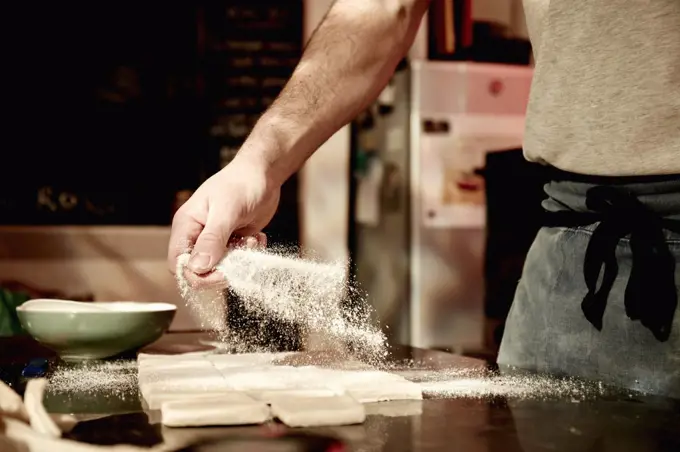 A baker working on a floured surface, dividing prepared dough into squares.