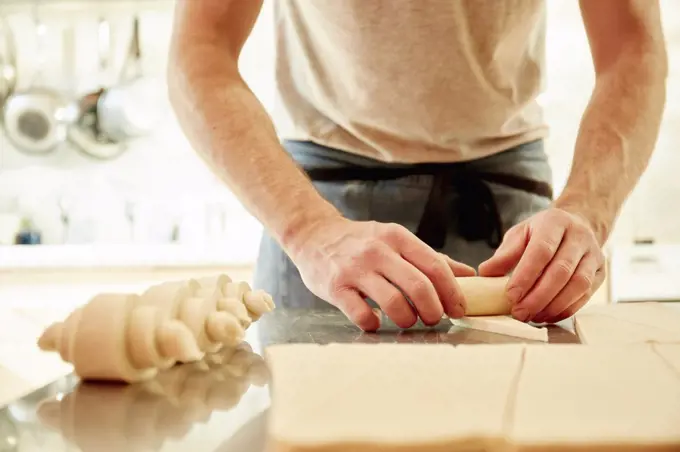 A baker working on a floured surface, rolling up dough squares into croissant shapes before baking.