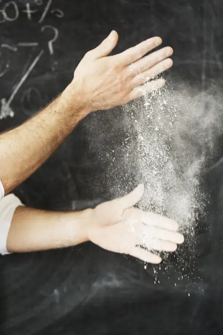 Close up of a baker standing in front of a blackboard, dusting his hands with flour.