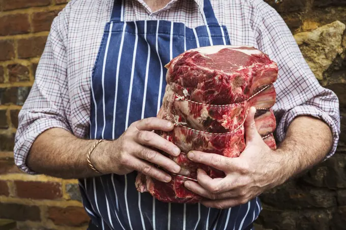 Butcher in blue striped apron holding a large piece of beef.