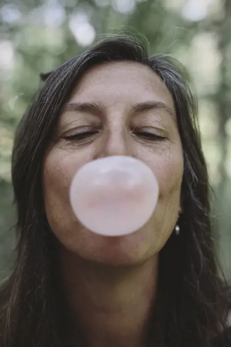 Portrait of middle aged woman blowing bubble gum bubble