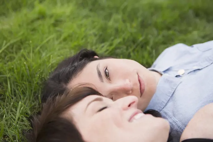 A same sex couple, two women lyiing on the grass, looking tenderly at each other, relaxing.