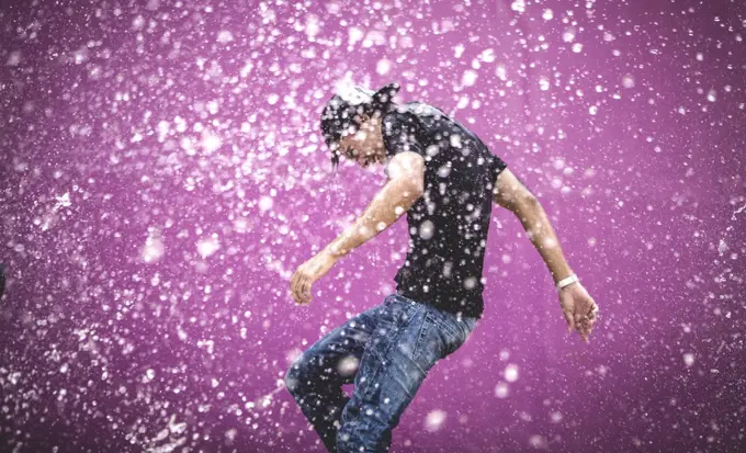 Young man standing in a shower of water drops.