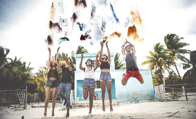 Young people standing on a beach throwing paint pigment into the air.