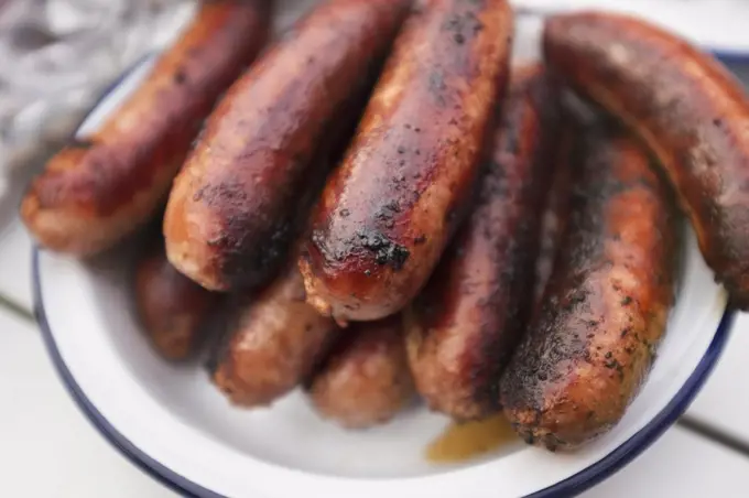 A tin plate stacked with cooked sausages on a table.