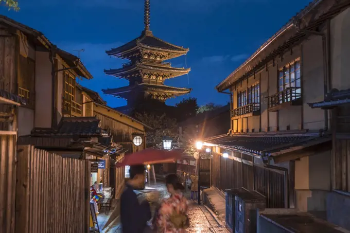 Japanese couple in traditional dress standing in a street at night, a pagoda in the background.