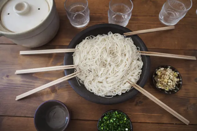 High angle close up of bowl with noodles and pairs of wooden chopsticks on a table.