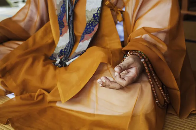 Close up of Buddhist monk wearing golden robe sitting cross legged on the floor, meditating, Buddhist hand gesture.