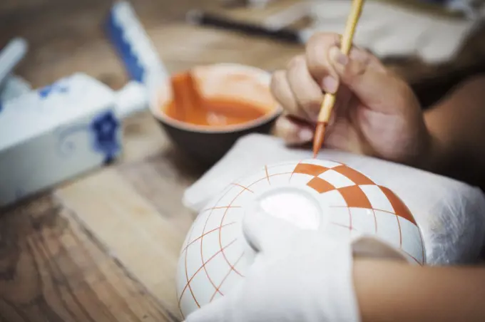 Close up of person working in a Japanese porcelain workshop, painting geometric pattern onto white bowls with paintbrush.