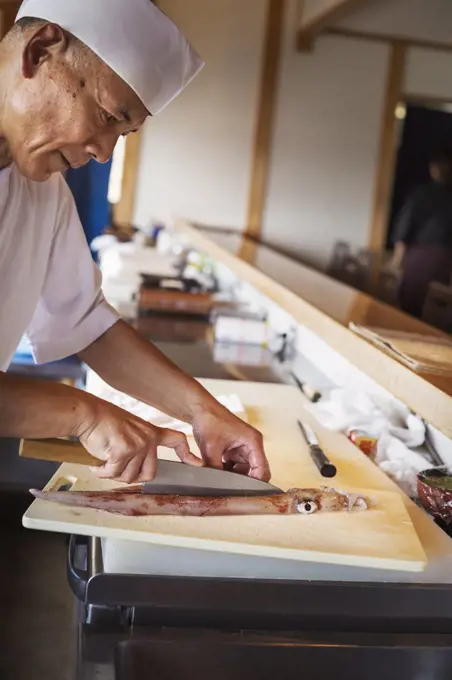 Chef working at a counter at a Japanese sushi restaurant, cutting a squid.