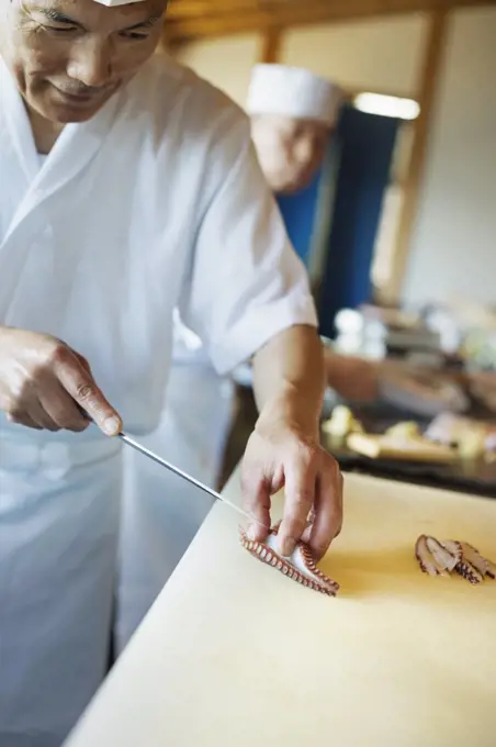 Two chefs working at a counter at a Japanese sushi restaurant, slicing octopus tentacle.