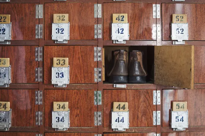 One pair of shoes in a shoe locker with an open door. Lockers in a row, with numbers.