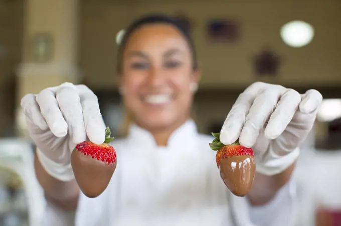 Hispanic woman holding a chocolate covered strawberry in a candy shop.