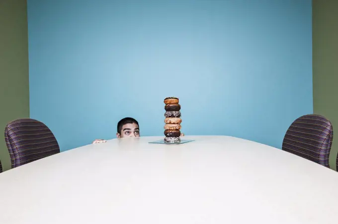 Businessman hiding behind a table with a stock of doughnuts on it.