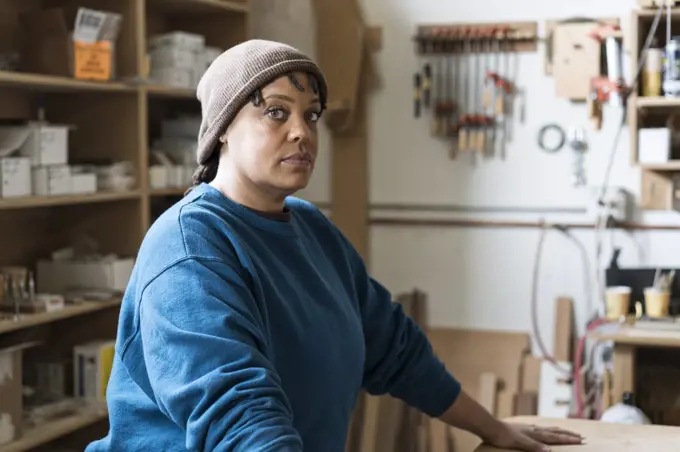 Portrait of a Black woman carpenter in a large woodworking shop.