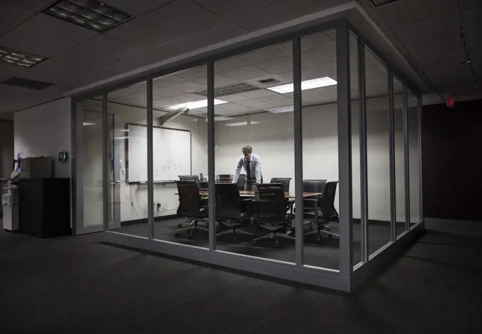 Caucasian businessman working at night in a glassed in conference room.